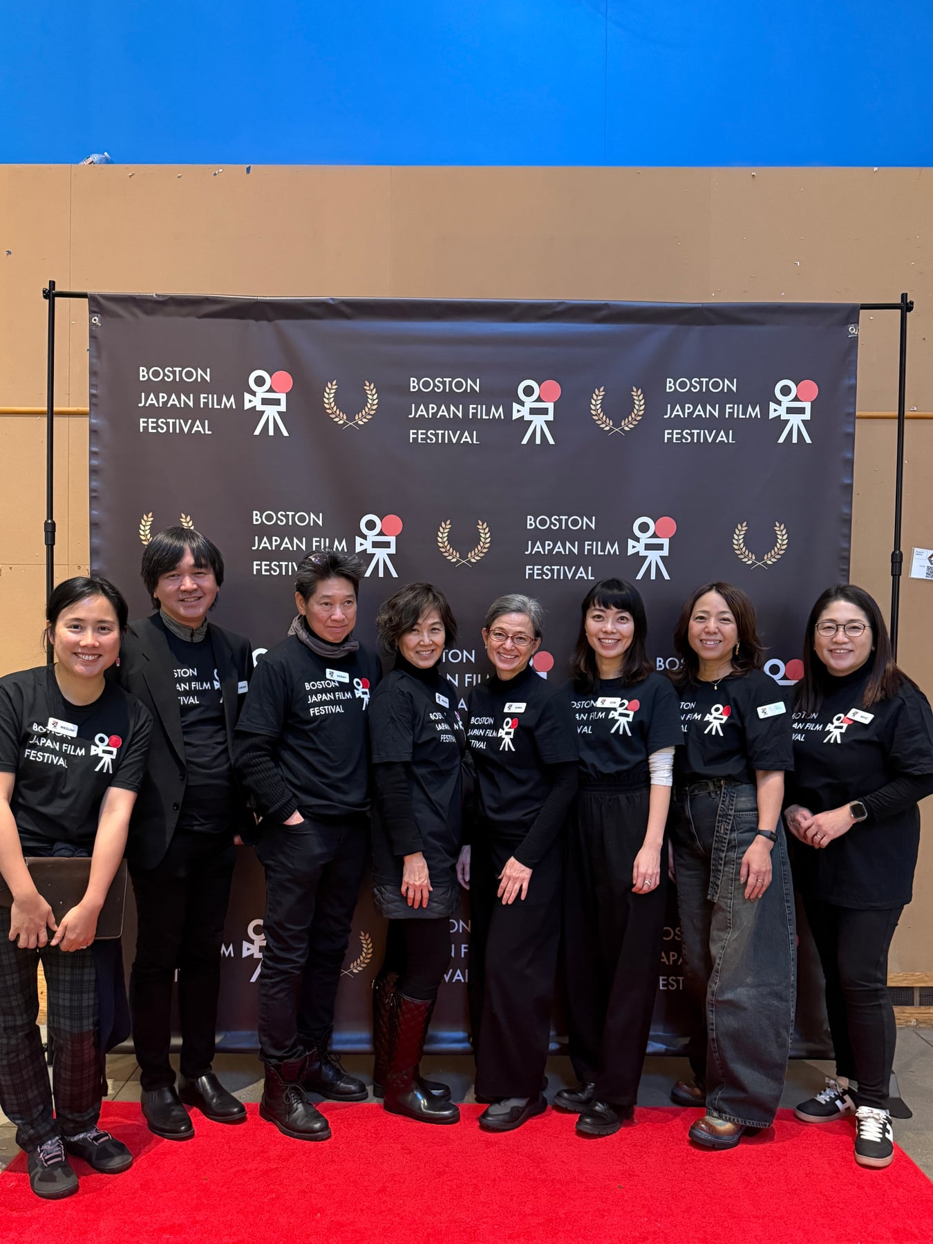 Boston Japan Film Festivalのバックドロップを背に、赤いカーペットに並ぶ8人の集合写真。